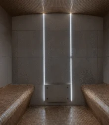 Warm tiled steam room with two family-friendly benches, tray of water and glasses, soft vertical lighting