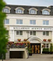 Family arriving at Killarney Avenue Hotel entrance, warmly lit façade with flower baskets and trees