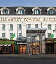 Family arriving at Killarney Towers Hotel entrance, warmly lit façade with flags and street café (80 characters)