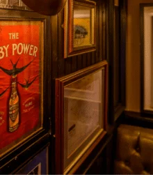 Warm pub interior with family seated beside framed vintage "The Baby Power" poster and artwork