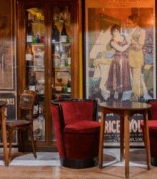 Cosy hotel lounge with family-style seating, vintage posters, wooden tables and red velvet chairs