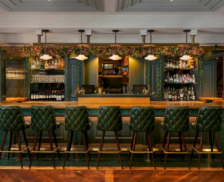 Elegant hotel bar with green leather stools and floral décor, inviting for families and groups.