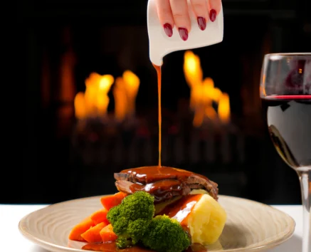 Elegant meal by the fireside with roast, vegetables, and wine.