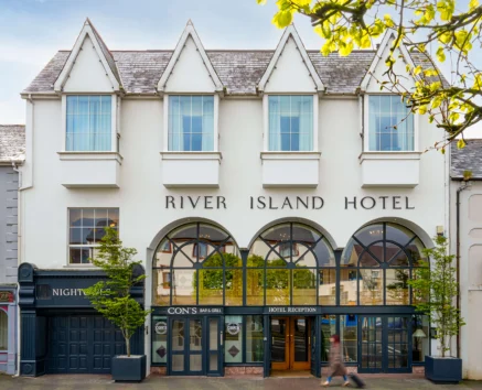 A charming, classic hotel facade with passersby, welcoming guests to the River Island Hotel.