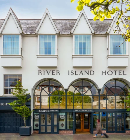 A charming, classic hotel facade with passersby, welcoming guests to the River Island Hotel.