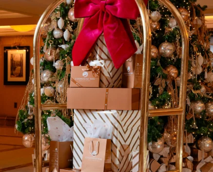 Christmas trolley with gifts and festive tree in hotel lobby.