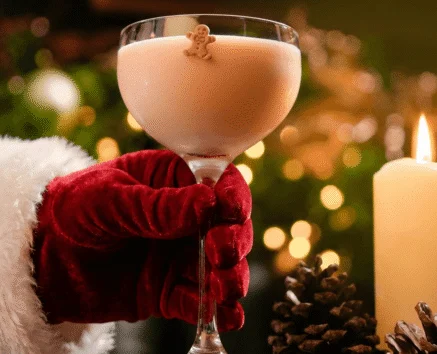 Santa's hand holding cocktail by candlelight with festive decor.