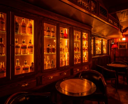 Cosy pub interior with warm lighting, wooden furnishings, and illuminated shelves of spirits.