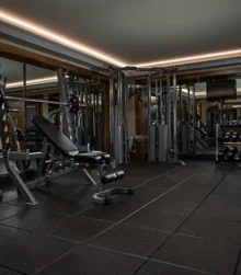 Modern hotel gym with family-friendly weight bench, dumbbells and mirrored walls, warm lighting (transcription: none visible)
