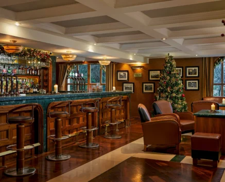 A cosy hotel bar decorated with Christmas lights and a tree, featuring wood interiors and plush seating.