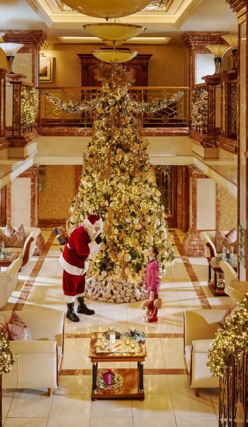 Family joy around a grand Christmas tree in a luxurious hotel lobby, adorned with festive lights.
