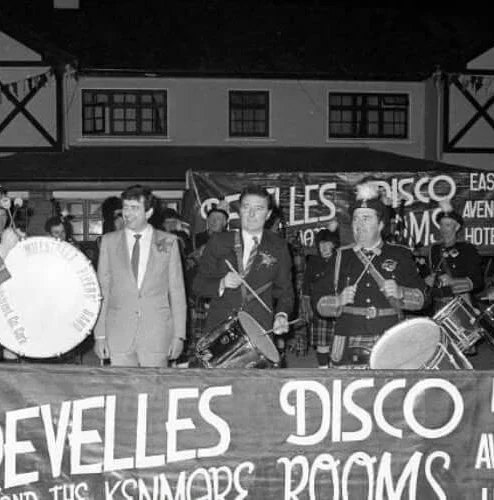 A group of musicians and a man in front of a hotel, enjoying live music.