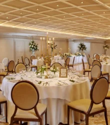 Elegant banquet hall set for a large gathering, featuring white tablecloths and floral centrepieces.