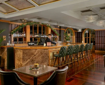 Elegant hotel bar with bartender, green chairs, and festive greenery.